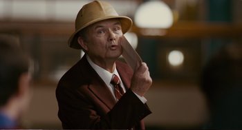 Movie still from “Cedar Rapids” (2011), directed by Miguel Arteta – An older man in a suit and hat holding a knife; Close Up shot, Over the shoulder angle