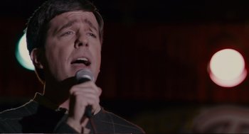 Movie still from “Cedar Rapids” (2011), directed by Miguel Arteta – A man is singing into a microphone in front of a dark background; Close Up shot, High angle