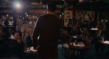 Movie still from “Cedar Rapids” (2011), directed by Miguel Arteta – A man standing in front of a group of people in a room; Wide shot, Over the shoulder angle