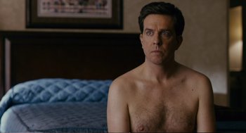 Movie still from “Cedar Rapids” (2011), directed by Miguel Arteta – A shirtless man sitting on top of a bed next to a bed; Medium shot, Over the shoulder angle