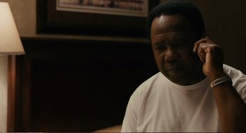 Movie still from “Cedar Rapids” (2011), directed by Miguel Arteta – A man in a white t - shirt sitting in front of a picture; Close Up shot, Over the shoulder angle