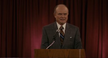 Movie still from “Cedar Rapids” (2011), directed by Miguel Arteta – A man standing at a podium speaking to a crowd; Medium shot, Over the shoulder angle