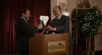 Movie still from “Cedar Rapids” (2011), directed by Miguel Arteta – Two men in business suits are holding a microphone; Medium shot, Over the shoulder angle