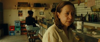 Movie still from “Central Station” (1998), directed by Walter Salles – An older woman sitting at a counter in front of a bar; Close Up shot, Over the shoulder angle