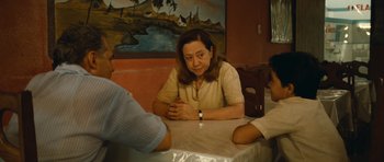 Movie still from “Central Station” (1998), directed by Walter Salles – A woman sitting at a table with two other people; Medium shot, Over the shoulder angle