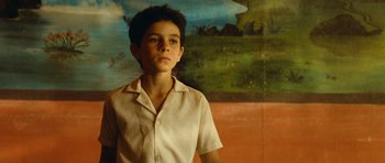 Movie still from “Central Station” (1998), directed by Walter Salles – A boy in a white shirt is standing in front of a painting; Medium shot, Low angle