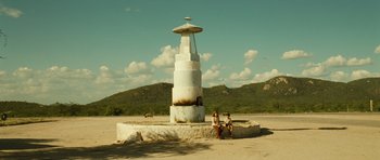 Movie still from “Central Station” (1998), directed by Walter Salles – Two people sitting on a rock in front of an outdoor structure; Extreme Wide shot, Low angle