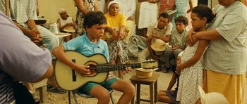 Movie still from “Central Station” (1998), directed by Walter Salles – A young man playing a guitar while others watch; Medium shot, Over the shoulder angle