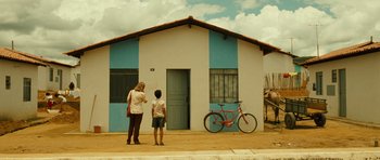 Movie still from “Central Station” (1998), directed by Walter Salles – Two people standing in front of a house with a bike parked in front of it; Wide shot, Low angle
