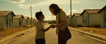 A woman and a young boy shaking hands on a street