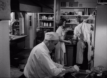 Movie still from “Champion” (1949), directed by Mark Robson – A group of people standing in a kitchen preparing food; Medium shot, Low angle