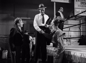 Movie still from “Champion” (1949), directed by Mark Robson – A man in a hat shaking hands with another man in a suit; Medium shot, Low angle