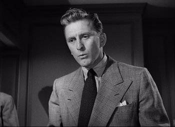 Movie still from “Champion” (1949), directed by Mark Robson – A man wearing a suit and tie in front of a wall; Close Up shot, Low angle