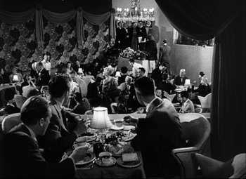 Movie still from “Champion” (1949), directed by Mark Robson – A black and white photo of people sitting at a table; Wide shot, High angle