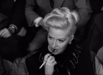 Movie still from “Champion” (1949), directed by Mark Robson – A black and white photo of a woman smoking a cigarette; Close Up shot, High angle