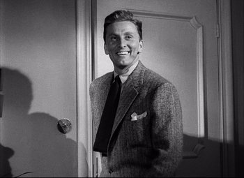 Movie still from “Champion” (1949), directed by Mark Robson – A man wearing a suit and tie smiling for the camera; Medium shot, Over the shoulder angle