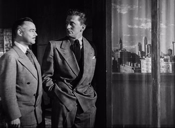 Movie still from “Champion” (1949), directed by Mark Robson – A couple of men standing next to each other in suits; Medium shot, Low angle