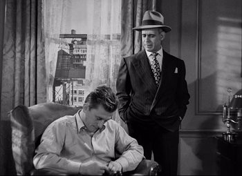 Movie still from “Champion” (1949), directed by Mark Robson – A man in a hat and a man in a suit standing next to a man; Medium shot, Over the shoulder angle
