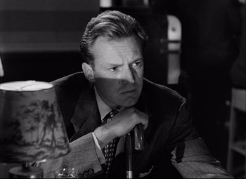 Movie still from “Champion” (1949), directed by Mark Robson – Black and white photograph of a man in a suit and tie looking pensive; Close Up shot, Over the shoulder angle
