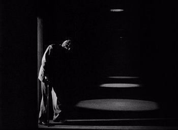Movie still from “Champion” (1949), directed by Mark Robson – A man standing in a dark room next to a wall; Wide shot, Low angle