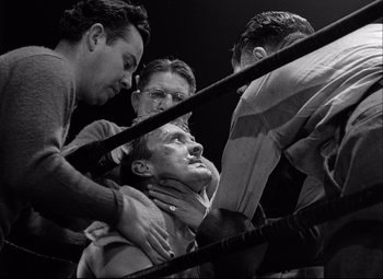 Movie still from “Champion” (1949), directed by Mark Robson – A group of men in a boxing ring with one man holding his head; Medium shot, Low angle