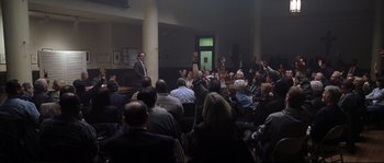 Movie still from “Changing Lanes” (2002), directed by Roger Michell – A group of people sitting in a large room; Wide shot, High angle