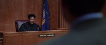 Movie still from “Changing Lanes” (2002), directed by Roger Michell – A woman sitting at a judge's desk in front of a microphone; Medium shot, Low angle