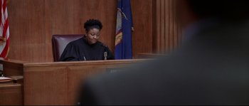 Movie still from “Changing Lanes” (2002), directed by Roger Michell – A woman sitting in front of a microphone in a courtroom; Medium shot, Over the shoulder angle