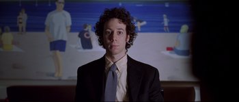 Movie still from “Changing Lanes” (2002), directed by Roger Michell – A man with curly hair wearing a suit and tie in front of a painting; Medium shot, Low angle