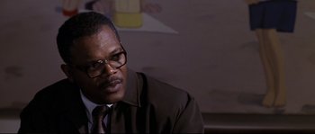 Movie still from “Changing Lanes” (2002), directed by Roger Michell – A man wearing a suit and tie sitting in front of a painting; Close Up shot, Over the shoulder angle