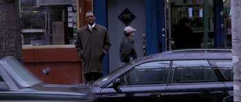 Movie still from “Changing Lanes” (2002), directed by Roger Michell – A man standing next to a car on a street; Wide shot, Low angle