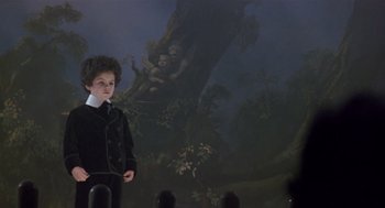 Movie still from “Chaplin” (1992), directed by Richard Attenborough – A young boy in a black suit standing in front of a painting; Wide shot, Low angle