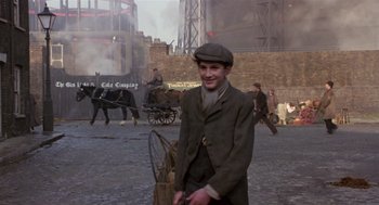 Movie still from “Chaplin” (1992), directed by Richard Attenborough – A man standing in the middle of a street holding an umbrella; Wide shot, Over the shoulder angle