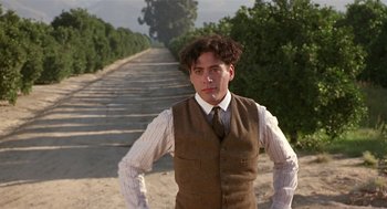 Movie still from “Chaplin” (1992), directed by Richard Attenborough – A man in vest and tie standing on the side of a road; Medium shot, Low angle