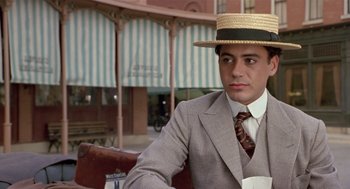 Movie still from “Chaplin” (1992), directed by Richard Attenborough – A man in a suit and straw hat sitting on a bench; Close Up shot, Over the shoulder angle