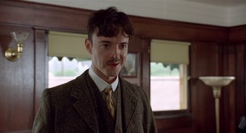 Movie still from “Chaplin” (1992), directed by Richard Attenborough – A man in a suit and tie standing next to a window; Close Up shot, Low angle