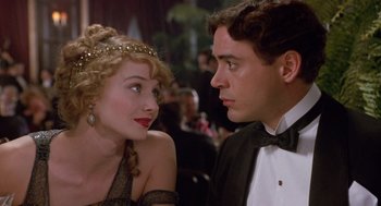 Movie still from “Chaplin” (1992), directed by Richard Attenborough – A man and a woman sitting next to each other at an event; Close Up shot, Over the shoulder angle