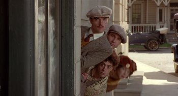 Movie still from “Chaplin” (1992), directed by Richard Attenborough – A group of men standing next to each other on a sidewalk; Medium shot, Low angle