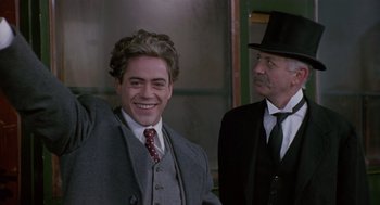 Movie still from “Chaplin” (1992), directed by Richard Attenborough – A man in a suit and a hat standing next to another man in a suit; Medium shot, Low angle