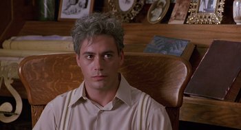 Movie still from “Chaplin” (1992), directed by Richard Attenborough – A man sitting in a chair in front of pictures; Close Up shot, Over the shoulder angle