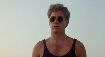 Movie still from “Chaplin” (1992), directed by Richard Attenborough – A man wearing a black tank top and yellow sunglasses; Close Up shot, Low angle