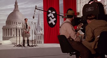 Movie still from “Chaplin” (1992), directed by Richard Attenborough – A man in a hat and a microphone on a stage; Wide shot, Low angle