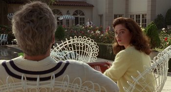 Movie still from “Chaplin” (1992), directed by Richard Attenborough – A man and a woman sitting on a chair in front of a house; Medium shot, Over the shoulder angle