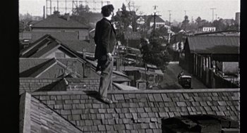 Movie still from “Chaplin” (1992), directed by Richard Attenborough – A man standing on top of a roof looking over a city; Wide shot, Low angle