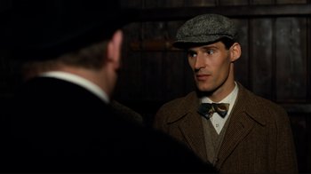 Movie still from “Chariots of Fire” (1981), directed by Hugh Hudson – A man wearing a hat and a bow tie talking to another man wearing a suit; Close Up shot, Over the shoulder angle