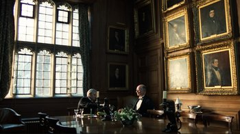 Movie still from “Chariots of Fire” (1981), directed by Hugh Hudson – Two men sitting at a table in front of a wall of pictures; Wide shot, High angle
