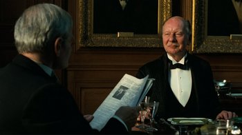 Movie still from “Chariots of Fire” (1981), directed by Hugh Hudson – An older man in a tuxedo sitting at a table with a glass of wine; Medium shot, Over the shoulder angle