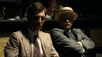 Movie still from “Chariots of Fire” (1981), directed by Hugh Hudson – Two men sitting next to each other wearing suits and hats; Close Up shot, Low angle