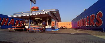 Movie still from “Charlie's Angels” (2000), directed by McG – A man standing outside of a sandwich shop on the side of the road; Extreme Wide shot, High angle