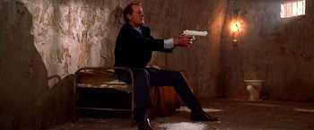 Movie still from “Charlie's Angels” (2000), directed by McG – A man sitting on a chair holding a gun; Medium shot, Low angle
